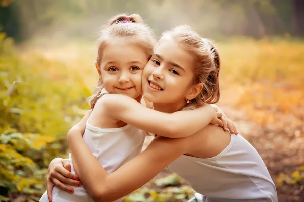 Concept d'enfance, de famille, d'amitié et de personnes - deux jeunes sœurs heureuses embrassant à l'extérieur . — Photo