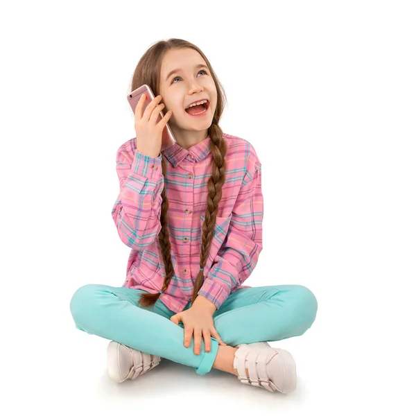 Joyeux petite fille avec téléphone intelligent assis sur le sol isolé sur fond blanc. Personnes, enfants, technologie Photo De Stock