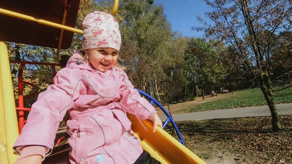 Güneşli bir günde parkta kayarken tatlı küçük kız eğleniyor.