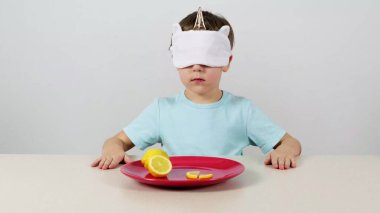 Maskeli küçük çocuk limonu deneyip tahmin ediyor.