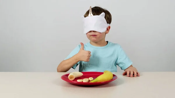 Little boy in a mask tries and guesses banan and gives thumbs up