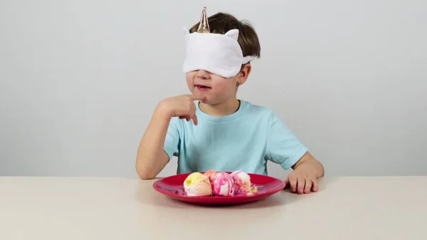 Maskeli küçük çocuk dondurma yemeye çalışıyor ve tahmin ediyor.