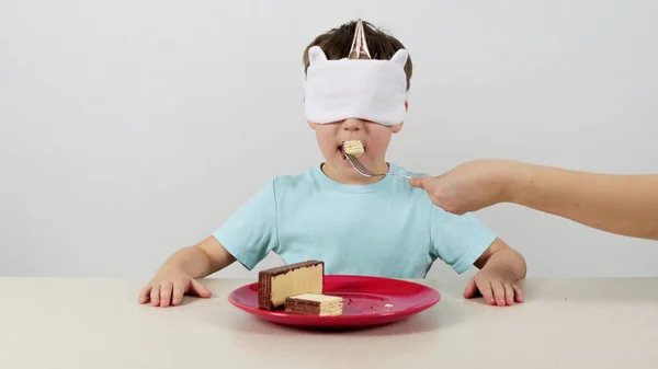 Maskeli küçük çocuk çikolatalı waffle deneyip tahmin ediyor ve baş parmağını kaldırıyor.