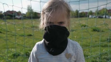 Siyah koruyucu maskeli tehditkar bakışlı bir kız futbol kalesinde duruyor. Sert bakışlı bir kaleci. Yavaş çekim
