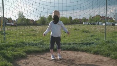 Siyah koruyucu maskeli bir kız futbol kalesinde duruyor ve ellerini çırpıyor. Yavaş çekim