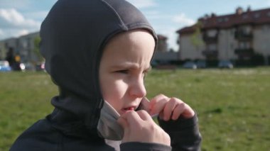 Ciddi görünüşlü bir çocuk dışarıda koruyucu maske takıyor. Yavaş çekim