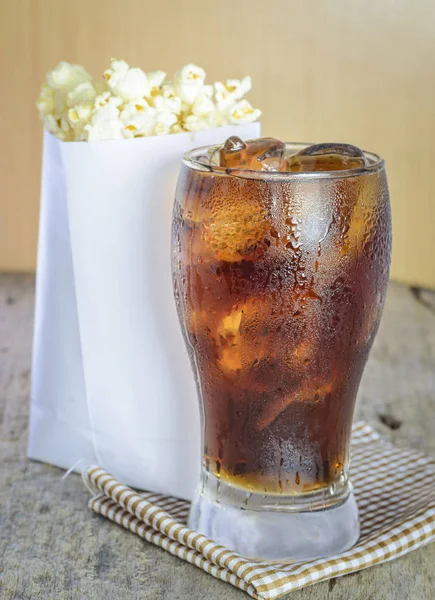 Cola con hielo y palomitas de maíz sobre una madera . —  Fotos de Stock