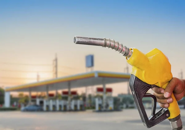 Holding a fuel nozzle against with gas station blurred backgroun — Stock Photo, Image