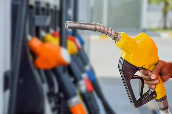 Houden van een brandstof-mondstuk tegen met een benzinestation wazig pagina — Stockfoto