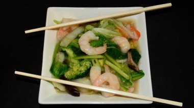 Beyaz bir tabakta sebzeli karides ve mantar.