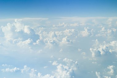 Mavi ufuk üzerinde büyük beyaz kümülüs bulutları, uçak penceresinden görüş..
