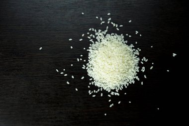 Koyu ahşap bir masada küçük bir pirinç yığını..