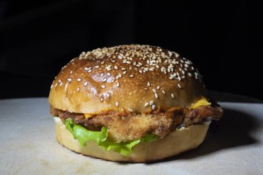 Kesme tahtasında tavuklu ve yeşil salatalı hamburger, siyah arka planda..