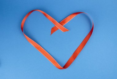 Red ribbon in the shape of a heart on a blue background.