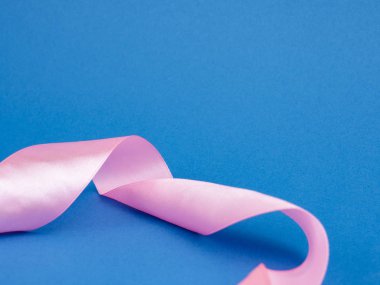 Close-up of a swirling pink ribbon on a blue background.