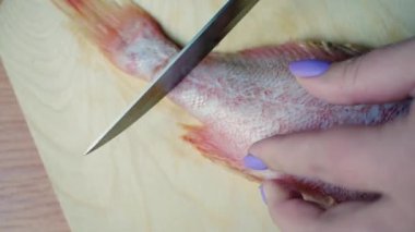 Female hands cut a raw fish with a knife.