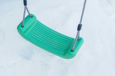 Beyaz kar arka planında yeşil plastik salıncak.