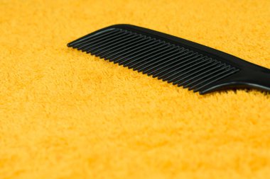 Sarı havlunun üzerinde büyük dişli siyah plastik bir saç fırçası var..