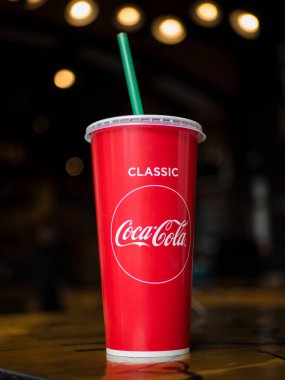 Khabarovsk, Rusya - 7 Mart 2020. Üzerinde Coca-Cola yazan kırmızı bir kağıt bardak ve yeşil pipetle koyu bir arka planda Bokeh..