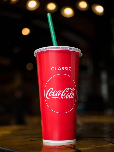 Khabarovsk, Rusya - 7 Mart 2020. Üzerinde Coca-Cola yazan kırmızı bir kağıt bardak ve yeşil pipetle koyu bir arka planda Bokeh..