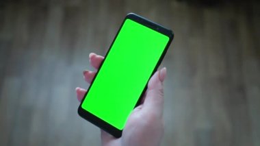 Beyaz bir kadın sağ elinde kapalı alanda krom anahtarı olan siyah bir akıllı telefon tutuyor..