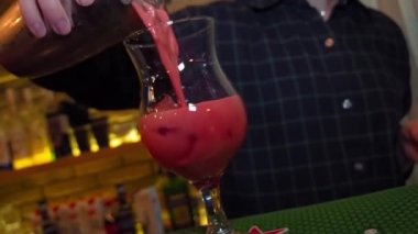 Yakın plan, beyaz bir kız kırmızı bir kokteyli şerbetli ve bir dilim portakallı bardağa dolduruyor..
