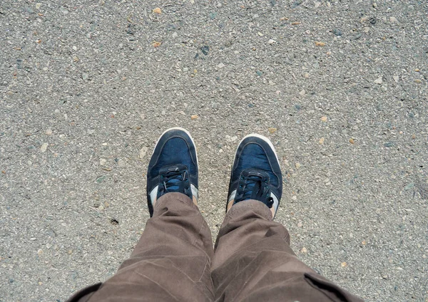 舗装上の茶色のパンツと青のスニーカーで男性の足のトップビュー — ストック写真
