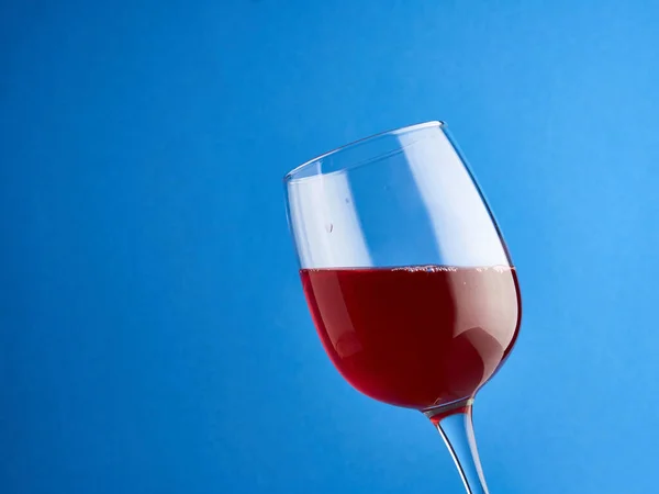 Red wine in a large glass goblet at an angle, on a blue background.