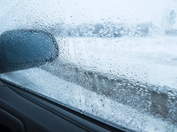Drops of water on the side window of the car, a mirror is visible in the frame.