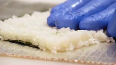 Mavi eldivenli bir aşçı Japon usulü pirinç, salatalık, peynir ve kırmızı balık hazırlar..