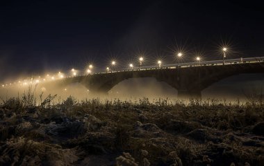 Kış. Buz. İyi geceler. Irkutsk şehrindeki Angara Nehri üzerindeki eski köprü. Fenerlerin yıldızları. Suyun üstünde sis var. Aşağıda boş alan.