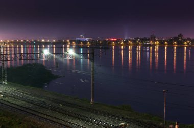 Yaz başları. Gece. Yağmurun altında, demiryolunun raylarını aydınlatan ve büyük nehrin kıyısından geçen ışıklar görülüyor. Karşıdaki kıyıda, istasyonun solundaki ışıklarda, şehrin ışıkları görülüyor..