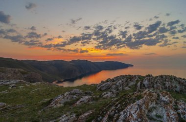 Doğu Sibirya. Baykal Gölü. Aya Körfezi. Pembe, turuncu, sarı sayısız kümülüs bulutu zümrüt ve mavi gökyüzünde yükselen güneş tarafından aydınlatılıyor. Güneşin ışıkları. Sudaki yansımalar.