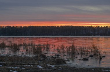 Sibirya 'da. Baykal bölgesi. Sonbaharın sonunda. Irkutsk Körfezi 'nin üzerinde güzel bir gündoğumu. Pembe, turuncu, sarı, suda mavi yansımalar. Çimlerin üzerindeki buz.