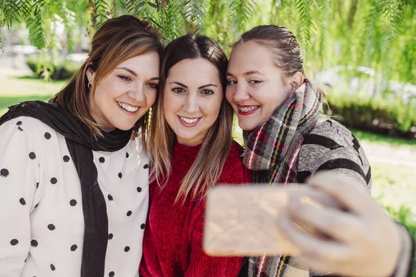 Üç gülümseyen arkadaş parkta selfie çekiyorlar. Sağ tarafta diş teli takan bir kız, yaşam tarzı konsepti.