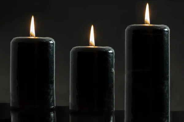 three black candles lit on a black background, esoteric concept