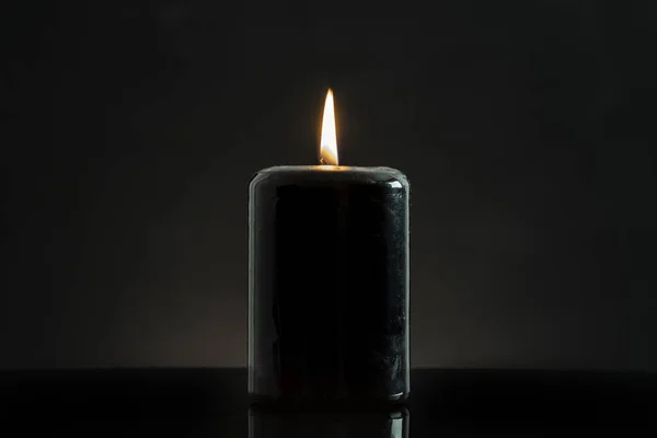 a black candle lit on a black background, esoteric concept