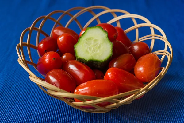 Fresh tomatoes with cucumber in a basket on a blue background — Stock Photo, Image