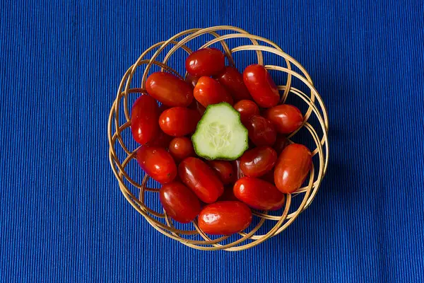 Tomates frescos con pepino en una canasta sobre un fondo azul — Foto de Stock