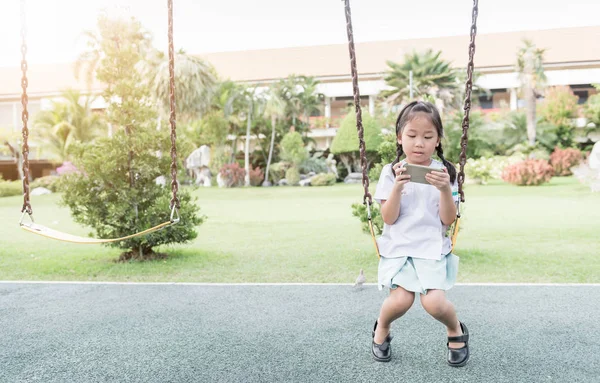 Bonito menina estudante jogar telefone inteligente no balanço — Fotografia de Stock