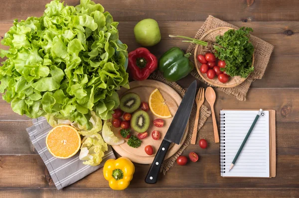 Verduras y frutas con cuaderno sobre fondo de madera — Foto de Stock