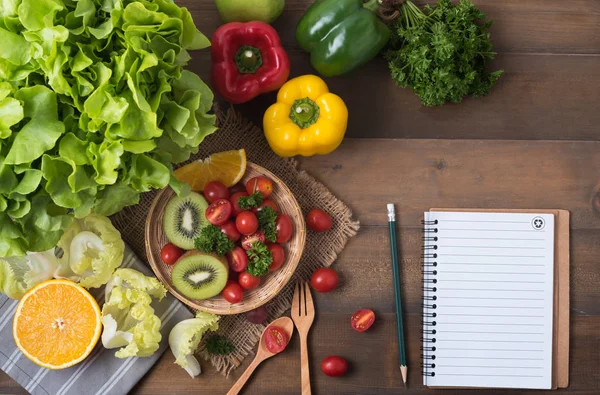 Verduras y frutas con cuaderno sobre fondo de madera — Foto de Stock