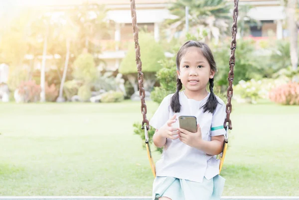 Carino ragazza studente giocare intelligente telefono su swing — Foto Stock