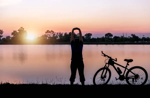 Sylwetka kobiety ćwiczenia w pobliżu rowerów na zachód słońca — Zdjęcie stockowe