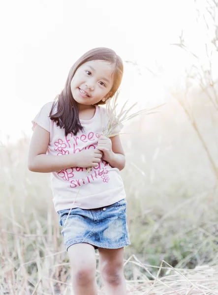 Carino ragazza sorriso e fiore erba in mano . — Foto Stock