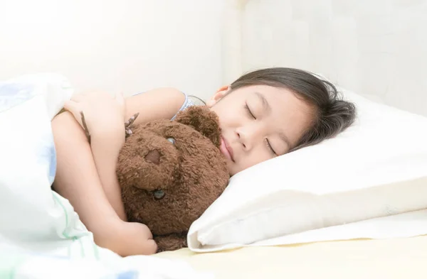 Ładna dziewczynka azjatyckich spać i przytul pluszowego misia na łóżku — Zdjęcie stockowe