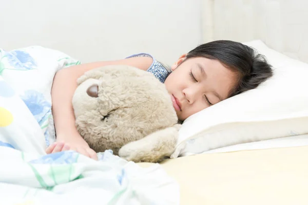 Süße kleine asiatische Mädchen schlafen und umarmen Teddybär auf Bett. — Stockfoto