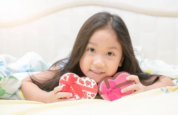 Chica sonrisa y acostarse en la cama con la caja de regalo de San Valentín . — Foto de Stock