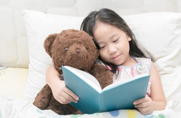 Mignonne petite asiatique fille en chemise de nuit lecture un livre avec teddy b — Photo