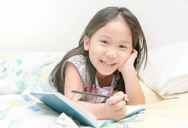 Ασιατικό χαριτωμένο κορίτσι χαμόγελο και εγγραφή σε ημερολόγιο στο κρεβάτι — Φωτογραφία Αρχείου